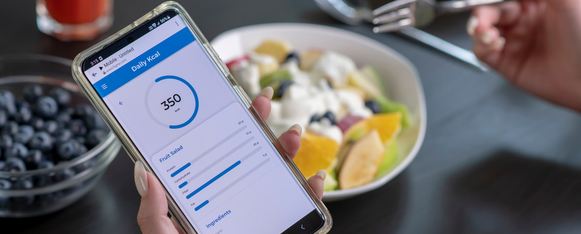 Person mit Früchtejoghurt. Diät-App auf Smartphone geöffnet.