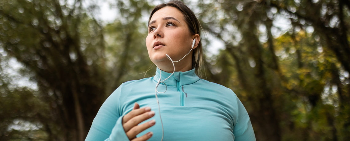 Übergewichtige Frau in Sportkleidung beim Joggen im Wald.