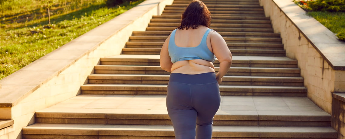 Übergewichtige Frau steigt erste Stufen einer Treppe hoch.